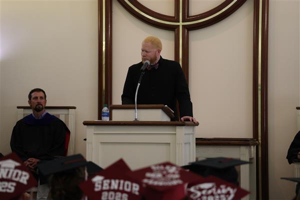 Donte Little stands at a podium during the Baccalaureate Ceremony while students in caps that read “Senior 2025” listen.